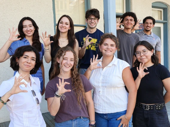 Nine of the ten 2025-2026 Mo's Policy Scholars flash Wildcat hand signs on the steps of the Udall Center